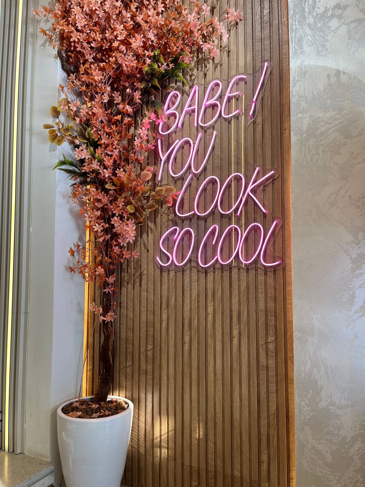 Le mur en tasseaux de bois de Roots 05, son enseigne néon et sa cascade de fleurs corail